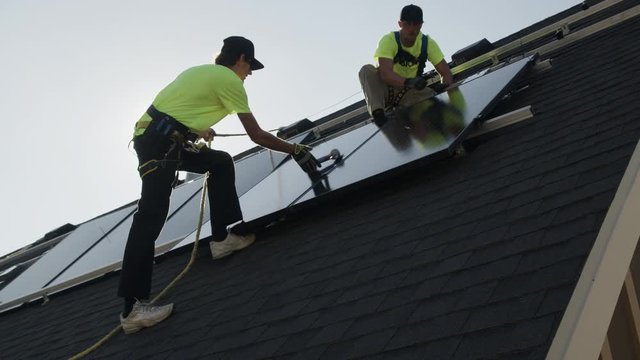 Medium panning low angle shot of workers installing solar panel on roof / Mapleton, Utah, United States