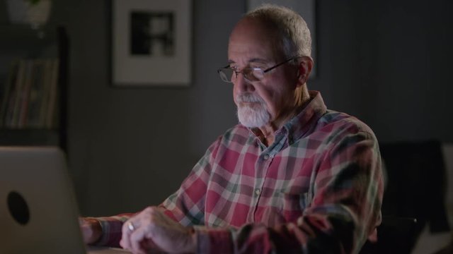 Close up panning shot of frustrated older man using laptop at night / Cedar Hills, Utah, United States