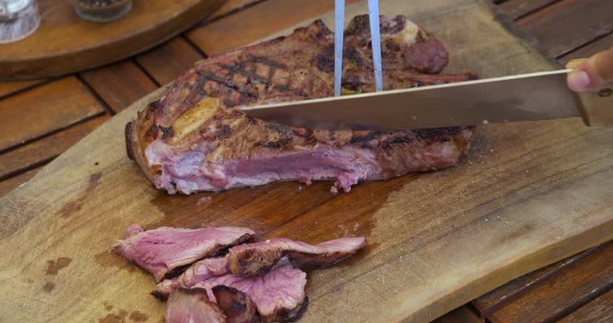 Cutting a grilled ribeye steak on a cutting board on wooden table.