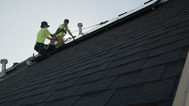 Wide panning low angle shot of workers installing solar panel on roof / Mapleton, Utah, United States