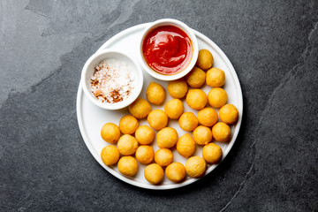 Fried potatoes ball, crocettes on white plate with tomato sauce, slate background, top view