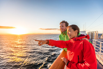 Cruise travel tourists couple pointing at sea view from ferry tour. Asian woman multiracial people traveling together at sunset.
