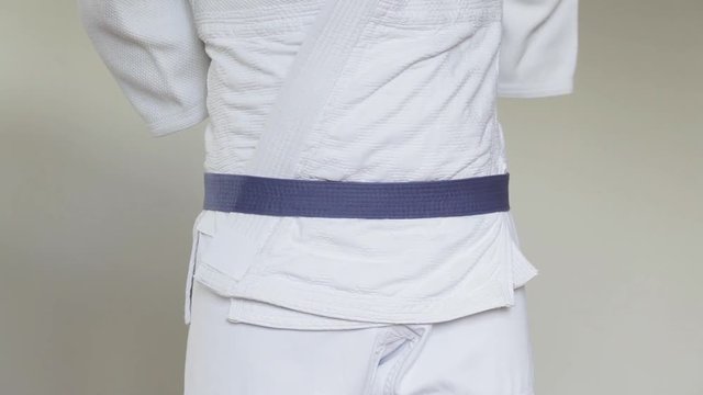 A young man in a white kimono shows how to tie a blue belt for judo, jiu zhditsu, sambo