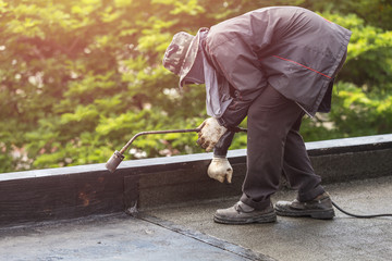 Group of worker installing tar foil on the rooftop of building. Waterproof system by gas and fire torching