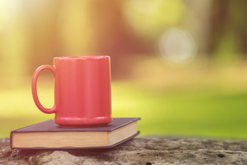 Red ceramic coffee cup and old book in green garden at morning time