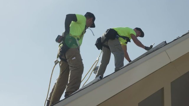 Medium panning low angle shot of workers installing rails on roof / Mapleton, Utah, United States