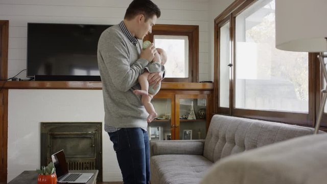 Medium shot of father walking while feeding bottle to baby daughter / Provo, Utah, United States