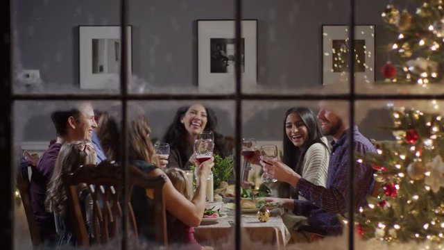 Medium zoom in shot of family toasting at meal on Christmas behind window / Cedar Hills, Utah, United States