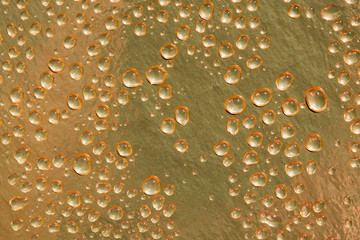 Abstract background. Large drops of water on a gold metal foil, top view. Macro.