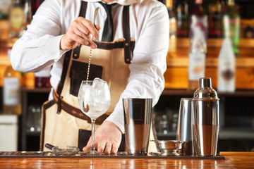 Bartender is mixing cocktail with spoon at bar counter background.