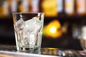 Closeup image of glass with ice cubes at bright bar counter background.