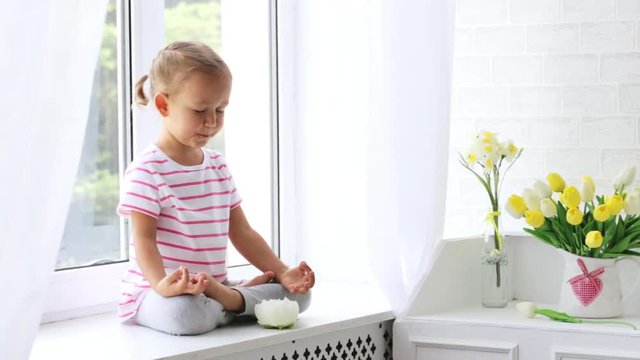 Little cute girl meditates on the window sill with beautiful natural light.