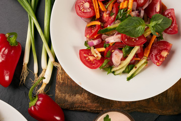 Fresh summer low-calories vegetable salad with tomatoes cucumbers carrots onions fresh bell peppers and garlic on wooden board over the dark stone background. Heathy vegetarian food and detox concept