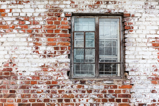 wooden window on weathered red brick wall painted white