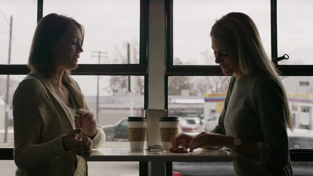 Medium shot of women eating cookie at table near window / Salt Lake City, Utah, United States