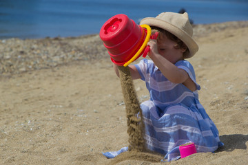 Little girl in a hat playing with sand on the beach