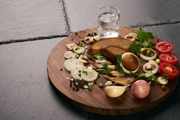 Traditional snacks salted herring with fresh vegetables, onion, bread, sprats and shot of vodka on...
