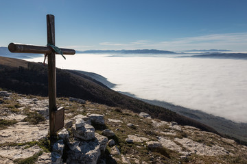 A wooden cross on top of a mountain, with a sea of fog below