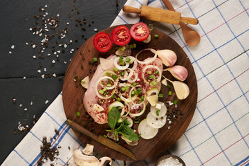 Raw chicken fillets with fresh vegetables on wooden cutting board over black stone background with copy space, top view