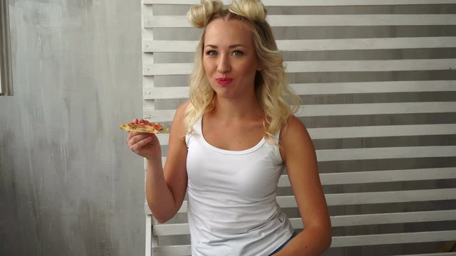 Young attractive girl eats pizza with delight. A hipster girl with a fashionable haircut is dressed in a white T-shirt.