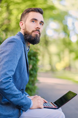 Fototapeta premium Handsome bearded male using laptop in a park.