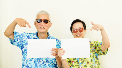 Senior Asian couple wearing holiday hawaii shirt holding white sign travel concept copy space