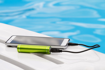 Smartphone connected to the green portable battery charger through USB cable on blue water...