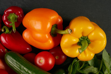 Fresh vegetables with greens on a black stone textured background. Healthy vegetarian eating.