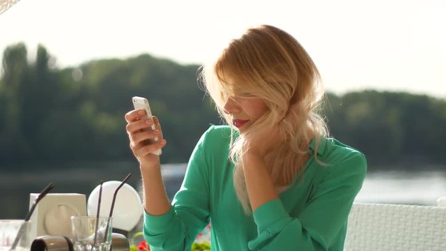 Smiling blonde girl with iPhone in cafe