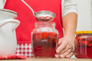 Housewife preparing a homemade strawberry jam in the glass jar for wintertime on the table in the kitchen. Tasty, sweet food from red berries.