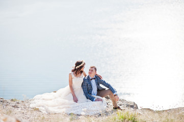 Stunning young wedding couple sitting on the edge of the cliff with a beautiful scenery on the background.
