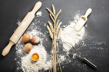 Background of egg wheat and flour next to cookwre on black background.