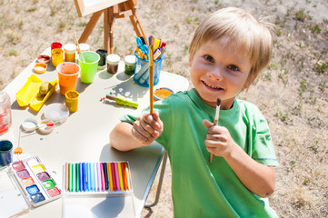 Little boy draws a picture near the house