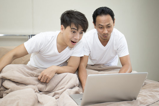 Man and friend watching porn movie with laptop in bedroom together.