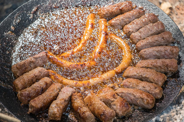 Minced meat sausages, kebabs, grilling on the vintage iron hot plate barbecue with grease bubbles surrounding them. Unhealthy eating, vintage methot of food preparation conceptual background