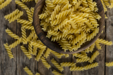 Pasta fusilli in a wooden bowl on wood background for healthy recipes.