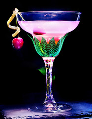 Cocktail tropical martini glass decoration by peel and green leaves. drink with cherry and mint leaf on black background.