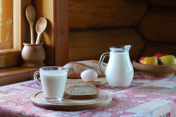 Village breakfast. A glass of milk, bread and fruit are on the table near the window in the rustic house.