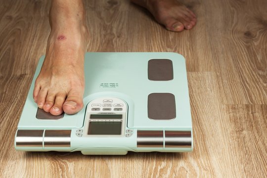 The old man is standing on a modern scale. Measuring the fat content of the body. Intelligent medical weight. The concept of obesity.