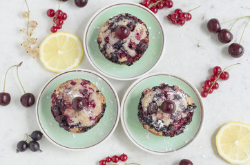 Three cupcakes with cherries and powder on a saucer decorated with fresh berries of currants and porridge. Collection
