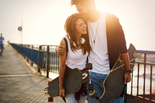 Picture of young attractive couple carrying skateboards