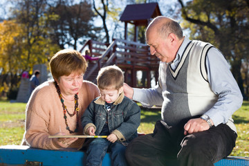 grandparents with grandson reading book in a park in autumn