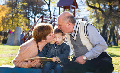 Fototapeta premium grandparents with grandson reading book in a park in autumn