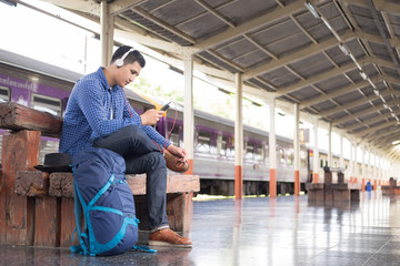 man traveler with backpacker listening to music at trainstation