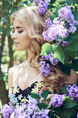 Outdoor fashion beautiful young woman surrounded by lilac flowers summer. Spring blossom lilac bush. Portrait of a girl blondes