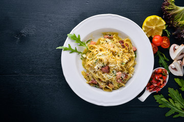 Pasta with bacon, cherry tomatoes, olives, and mushrooms with parmesan cheese. Italian food. On a black wooden surface. Free space for your text. Top view.