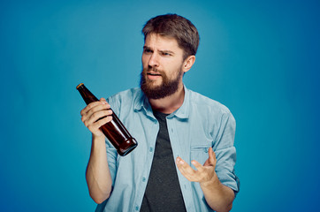 A young guy with a beard on a blue background holds a bottle of beer