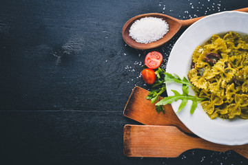 Pasta with spinach, olives and mushrooms with parmesan cheese. Italian food. On a black wooden surface. Free space for your text. Top view.