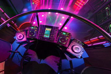 DJ mixing music on console at the colorful interior of european stylish night club with bright lights with disco mirror ball