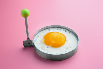 Fried sunny side up egg in round mold on colour background